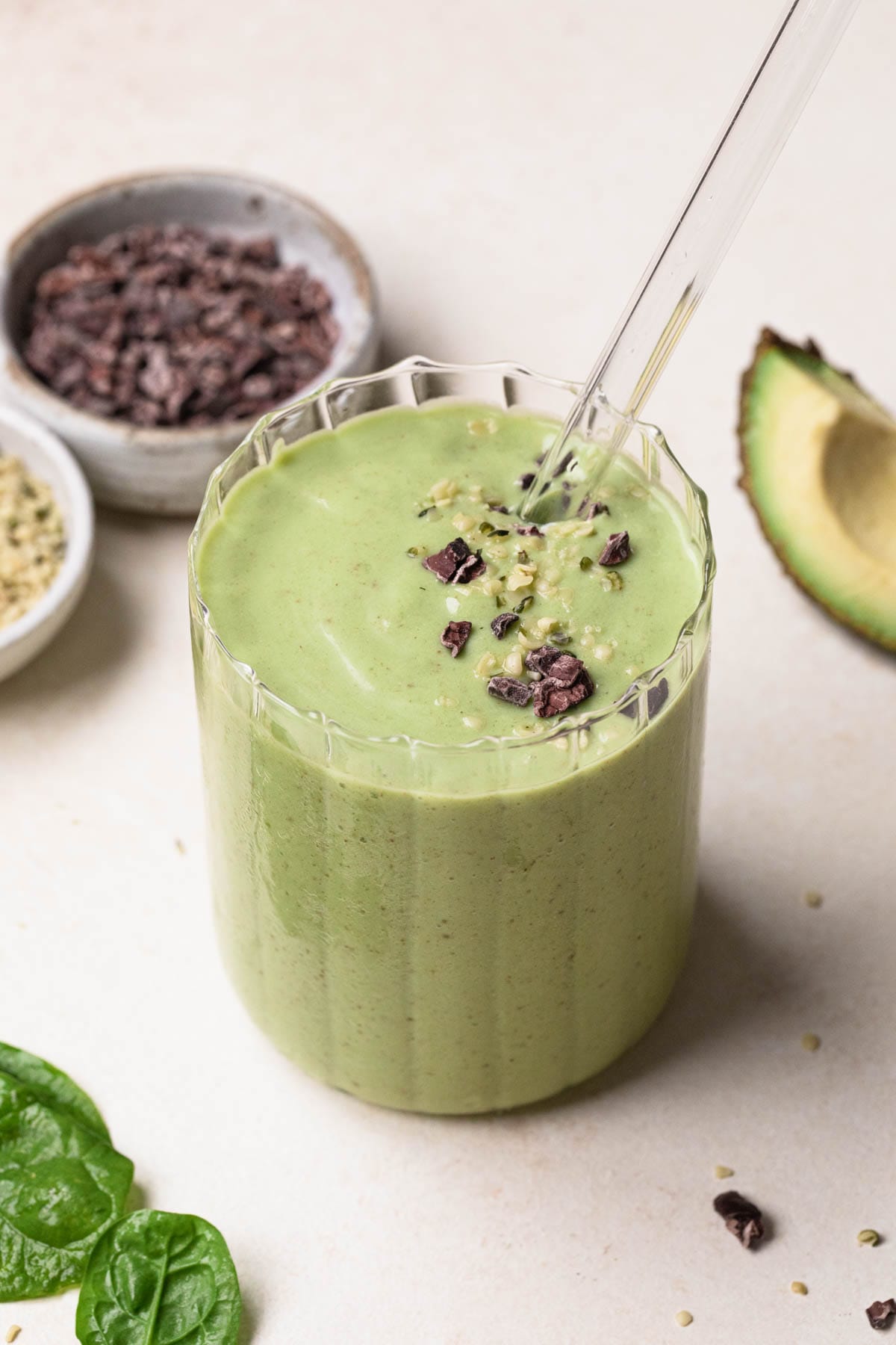 Avocado, banana and spinach green smoothie in a clear glass with a glass straw